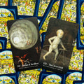 Tarot kortos rinkinio dvi atverstos kortos su meniniais tamsiais piešiniais ir ryškiai mėlynais nugarėliais, skirtos prekės peržiūrai