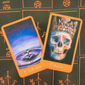 Tarot kortos komplektas, dvi priekinės kortos: 14 Temperance mėlyna vandens scena ir 13 Death kaukolė su oranžiniu rėmeliu, kontrastingos priežastys galerijoje