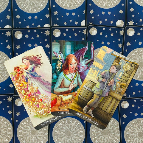 Tarot kortos — Pentaklių rinkinys: trys atverstos kortos (Karalienė, Riteris, Puslapis) ant mėlyno žvaigždėto nugarėlio, artimas kampas