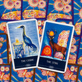 Tarot kortos dviejų kortų išklotinė su „The Crane“ ir „The Stag“ mėlynomis iliustracijomis ir spalvingu kortų fonu