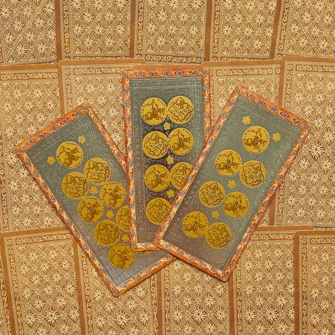 Tarot kortos su auksinėmis monetų emblemais, pilkais laukeliais ir oranžiniu ornamentu, trijų kortų išdėstymas