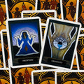 tarot kortos su dviem atverstomis kortomis: mėlyna Deception figūra ir gelsva Creativity taurė ant aukso‑juodo ornamentuoto fono