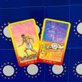 Tarot kortos su geltonu rėmeliu — Ugnies rūšies X ir IX kortos, nufotografuotos iš viršaus ant mėlyno žvaigždėto fono