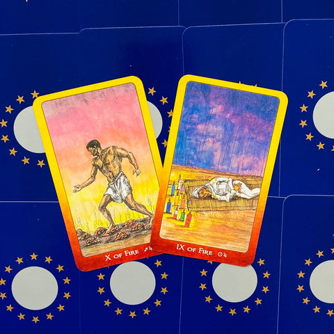 Tarot kortos su geltonu rėmeliu — Ugnies rūšies X ir IX kortos, nufotografuotos iš viršaus ant mėlyno žvaigždėto fono