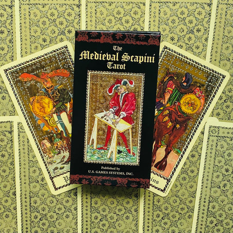 tarot kortos Medieval Scapini: juoda pakuotė su auksiniais užrašais ir dviejų kortų vėduoklė su viduramžių iliustracijomis