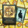 Orakulo kortos Animal Dreaming dėžutėje (Scott Alexander King), šalia atversta varnos/šnibždėtojos korta ant geltono simetriško fono