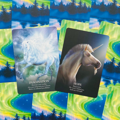 Kortos su vienaragiais — dvi oracle kortos „Imagination“ ir „Hope“ ant ryškaus žali‑mėlyno auroros fono, priekinių kampų vaizdas