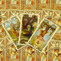 tarot kortos Art Nouveau stiliaus — trys atverstos kortos fanuotos centriniame kadre, auksiniai rėmai ir raštuotas nugarėlis