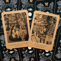 Taro kortos su rudos smėlio bordiūromis, dvi iliustruotos kortos (Artemis, The Creatrix) arti ant juodo ornamentuoto fono, atverstas poros variantas