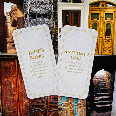 Orakulo kortos, dvi baltos su auksiniu šriftu (Jude's Song ir Anthony's Call) prieš durų koliažą
