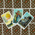 Tarot kortos Rider–Waite stiliaus trys atverstos kortos (Pentaklių tūzas, Karalius taurėse, Karalienė taurėse) ant raštuotos galinės pusės, matomas artimas kampinis išdėstymas