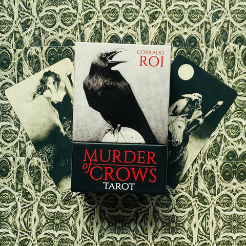 Tarot kortos Murder of Crows (Corrado Roi) – juoda-raudona dėžutė su varnų piešiniu centre ir dviem atverstomis kortomis fone