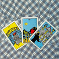 tarot kortos Rider–Waite, trys atvertos taurės kortos išdėstytos iš viršaus ant mėlyno raštuoto fono, pabrėžiant priekinį iliustracinį dizainą ir ryškias spalvas