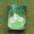 Earth Wisdom oracle kortos, žalia dėžutė su mistiniu miško viršeliu, nufotografuota iš priekio ant keltų kortų fono
