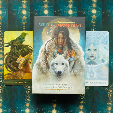 Orakulo kortos Wild Woman Rising dėžutė su baltu vilku ir moters viršeliu, dvi atvertos kortos šonuose ant tamsiai žalsvo ornamentuoto fono