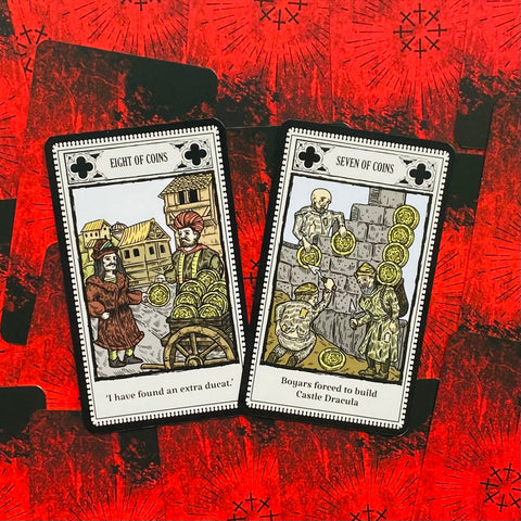 tarot kortos su monetų rūšimi, dvi atverstos kortos — Aštuoni ir Septyni monetų, padėtos ant ryškiai raudonos nugarėlės