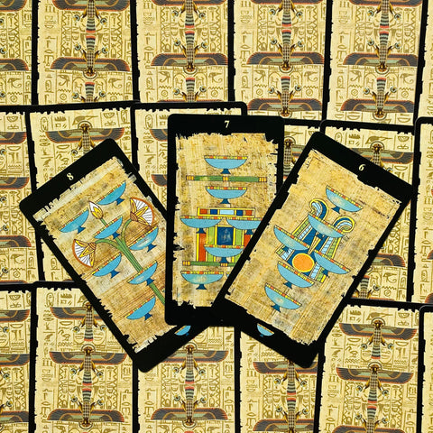 tarot kortos egiptietiško papiruso dizaino, trys atverstos kortos (6, 7, 8) su mėlynomis taurėmis ant juodo rėmo, fone kortų nugarėlėsTRGL