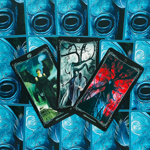 Tarot kortos su mėlynomis nugarėlėmis, trys atverstos kortos centre su tamsios fantastikos iliustracijomis, kampu išdėstytos
