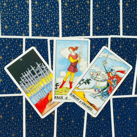 Tarot kortos Rider‑Waite stiliaus, trijų kardų kortų išklotinė (Dešimt kardų, Kardų Puslapis, Kardų Riteris) ant mėlynos žvaigždėtos nugarėlės