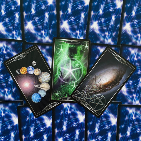 Tarot kortos kosminėmis mėlynomis nugarėlėmis, trys atverstos kortos su žaliu pentaklių simboliu, spiraline galaktika ir planetų motyvais
