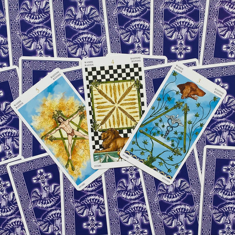 Tarot kortos – trys atvertos Rider‑Waite stiliaus kortos centre su liūtu, ugnimi ir lazdų motyvais, violetinė nugarėlė
