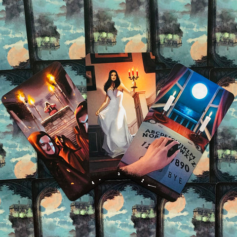 Tarot kortos su trimis atverčiamais dizainais — vaiduoklių ritualas, balta figūra prie žvakidės ir Ouija lenta, rodomos iš priekio