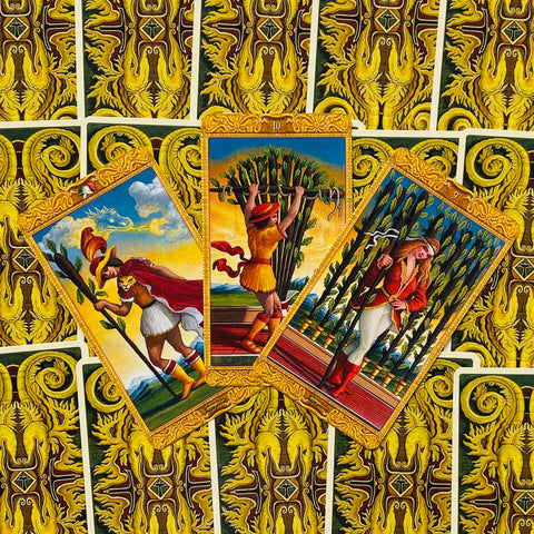 Tarot kortos – trijų kortų išklotinė su auksinėmis nugarėlėmis, šviesios spalvos Lazdų kortos parodytos centre ir šone