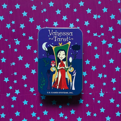 Tarot kortos Vanessa Tarot metalinėje mėlynoje dėžutėje, uždarytos centre ant violetinio fono su mėlynomis žvaigždėmis