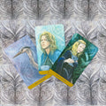 tarot kortos trys atverstos kortos su melsvais ir žaliais portretais (Ace of Swords, Queen of Cups) ant ornamentinės pilkos nugarėlės
