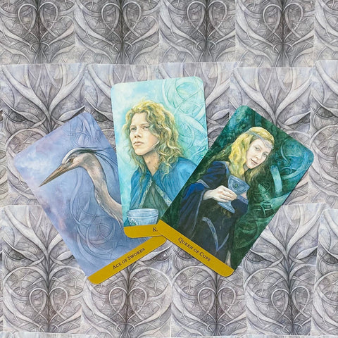 tarot kortos trys atverstos kortos su melsvais ir žaliais portretais (Ace of Swords, Queen of Cups) ant ornamentinės pilkos nugarėlės