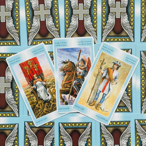 Tarot kortos, atverstos mėlyna nugarėle — Lazdų kostiumo Karalienė, Riteris ir Pustonis, kampu išdėstytos, parodytos prie dekoratyvinių nugarėlių