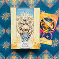 Seeker Oracle kortų rinkinys (Ravynne Phelan), kremine dėže su baltu tigro piešiniu ir viena spalvota korta šone, tamsiai turkio fone
