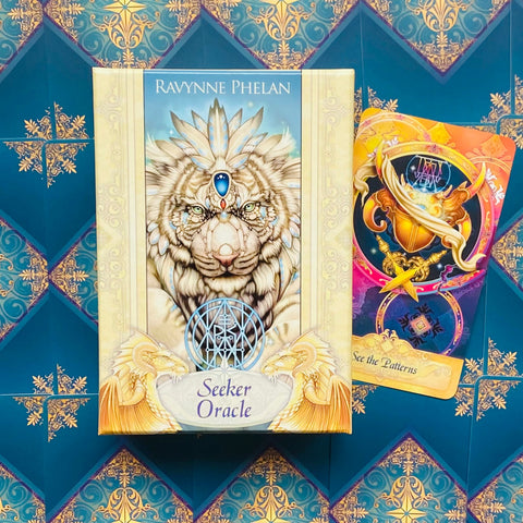 Seeker Oracle kortų rinkinys (Ravynne Phelan), kremine dėže su baltu tigro piešiniu ir viena spalvota korta šone, tamsiai turkio fone