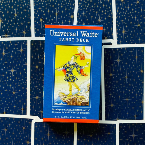 Universal Waite mėlyna tarot kortų dėžutė, priekinis vaizdas, padėta ant išdėstytų žvaigždėtų kortų nugarėlių kaip produkto nuotrauka