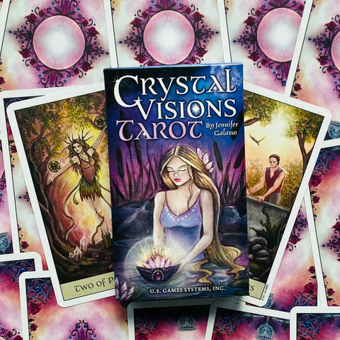 Tarot kortos „Crystal Visions“ dėžutė su violetiniu viršeliu ant paskleistų kortų, matomi keli atviri kortų paveikslai ir autoriaus vardas
