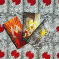 tarot kortos — trys atviros kortos su auksiniais ir raudonais akcentais, kampu išdėstytos ant raudono‑pilko raštuoto fono