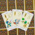 tarot kortos Wands, atverstos 10–9–8 kortos su linksmomis nykštukų iliustracijomis ir ornamentuotu nugarėlių raštu