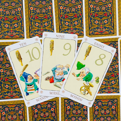 tarot kortos Wands, atverstos 10–9–8 kortos su linksmomis nykštukų iliustracijomis ir ornamentuotu nugarėlių raštu