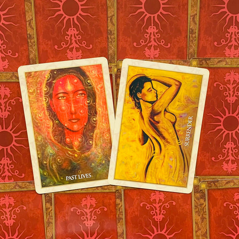 tarot kortos – dvi atverstos kortos (Past Lives raudonas portretas, Surrender geltona figūra) ant raudonų ornamentuotų nugarėlių