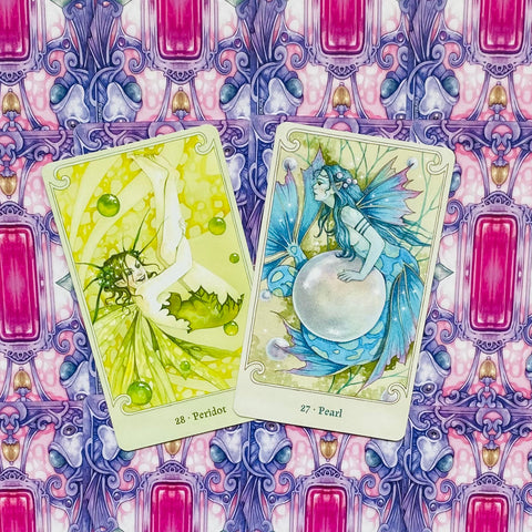 Orakulų kortų rinkinys su žalia Peridot ir mėlyna Pearl kortomis, pasvirusios ant rožinės‑violetinės ornamentinės fono tekstūros
