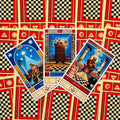 tarot kortos, atverstos trys kortos (Žvaigždė, Bokštas, Velnio) ant raudono‑juodo šachmatinio nugarėlės fono