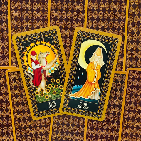 Tarot kortos su aukso rėmeliais, rodančios The Sun ir The Moon kortas ant raštuoto bordo fono, skirtos aiškinimui
