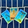 Tarot kortos Rider–Waite stiliaus su tamsiai mėlynomis nugarėlėmis, trijų kortų išdėstymas atverstas (Ace of Cups, King of Swords, Two of Cups), rodantis kortų priekį ir detales