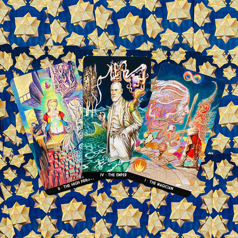 Tarot kortos trys – Būrėjas, Imperatorius ir Aukštoji Kunigė atverstos ant mėlyno audinio su auksinėmis žvaigždėmis, skiriasi iliustracijomis ir spalvomis