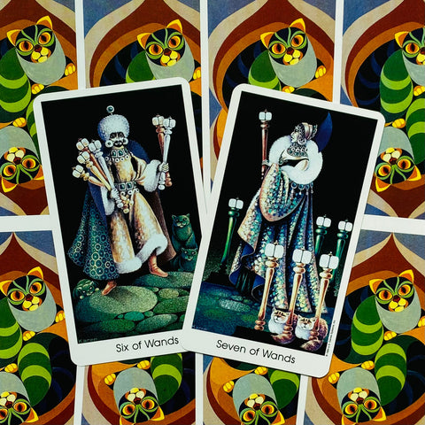 Tarot kortos su šešiomis ir septyniomis lazdomis, dvi kortos išdėstytos ant ryškaus katės rašto fono