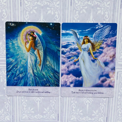 Angelų kortos, dvi atidarytos kortos šalia: mėlyna "Release" su aureole ir rožiniai‑melsvi "Rejuvenation" debesų dizainai