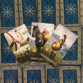 tarot kortos vikingų stiliaus rinkinys, trys atverstos kortos (Knight of Pentacles, Page of Pentacles) ant mėlyno ornamentuoto fono