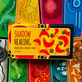 Shadow Healing kortų rinkinys geltonas viršelis su raudonais ornamentais, autorius Mel Brown, fotografuota iš viršaus, išryškėja dėžutės priekinė dalis