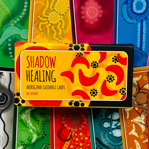 Shadow Healing kortų rinkinys geltonas viršelis su raudonais ornamentais, autorius Mel Brown, fotografuota iš viršaus, išryškėja dėžutės priekinė dalis