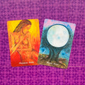 Oracle kortos: dvi iliustruotos kortos — oranžinė Physical Body ir mėlyna Moon Tree, padėtos ant violetinio raštuoto fono, rodomas poros kortų variantas